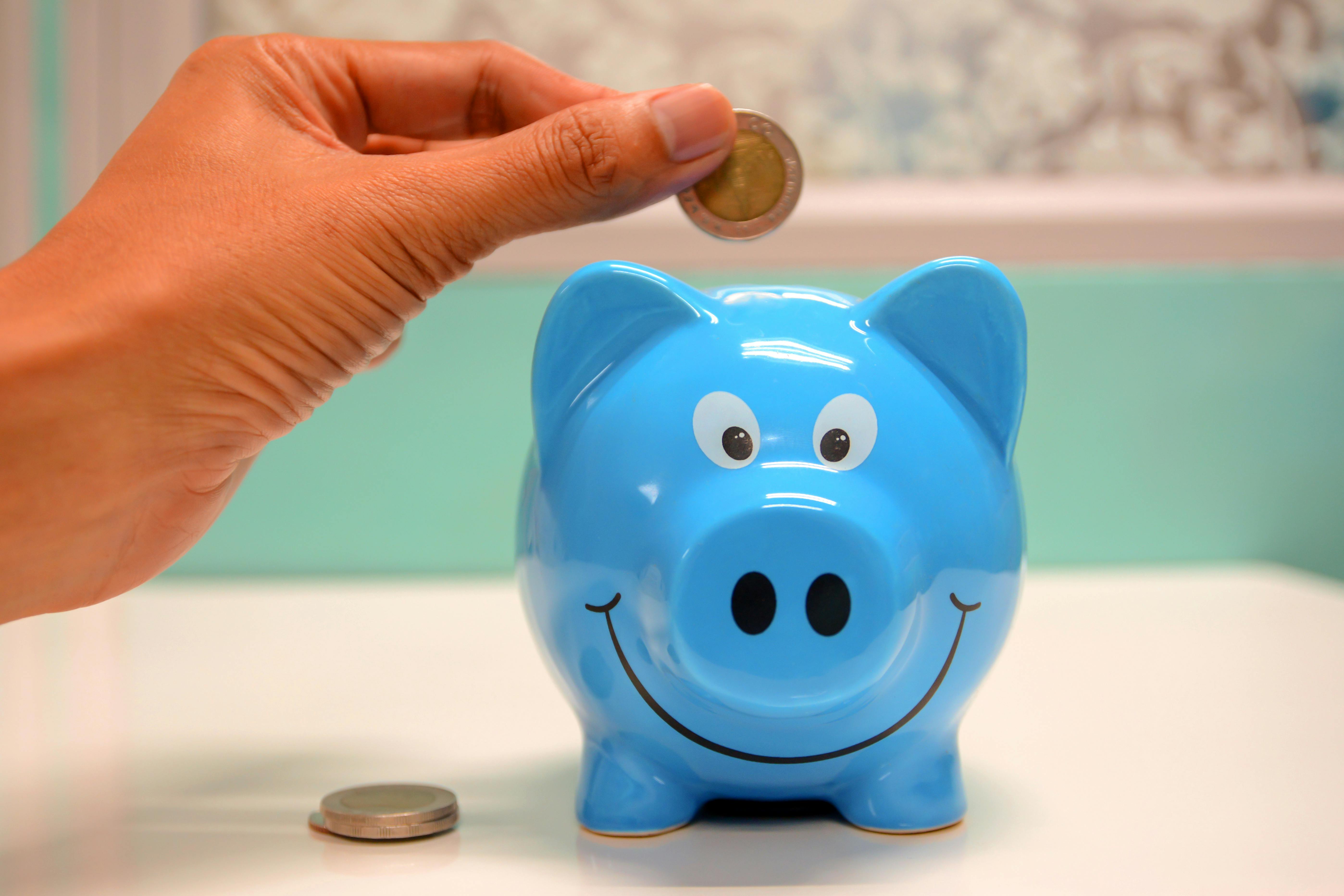 someone putting coins into a blue piggy bank