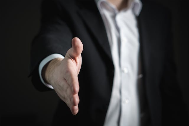 man in black suit holding out hand for handshake